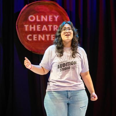 A high schooler, with one arm outstretched, performing a song 