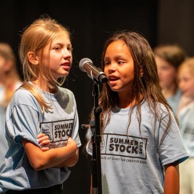 Two young kids singing together at a microphone