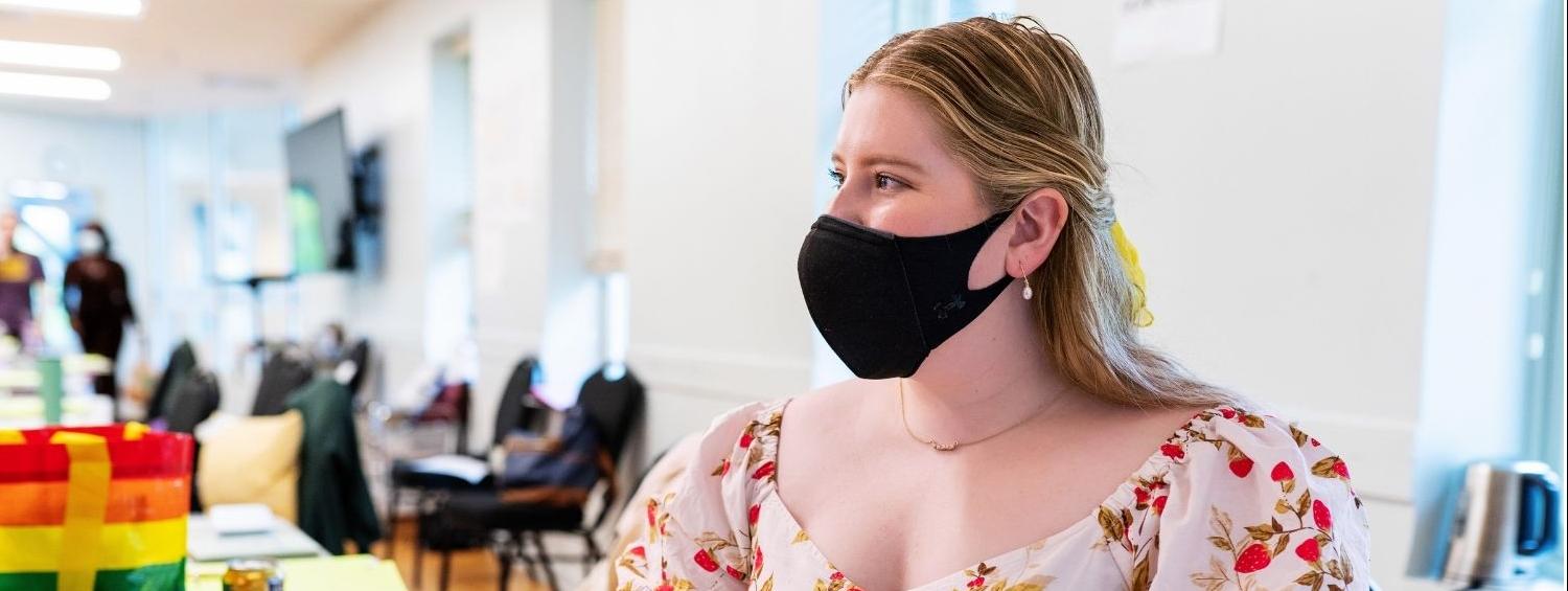 Image of Dramaturg Alissa Klusky (masked) sitting at a table with the script for The Joy that Carries You, she is smiling